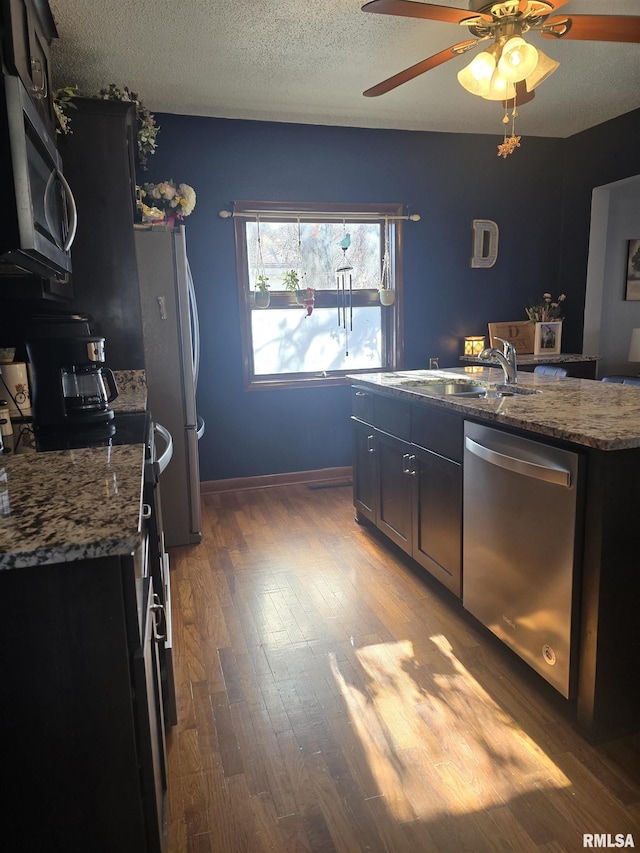 kitchen featuring stone counters, appliances with stainless steel finishes, hardwood / wood-style floors, sink, and a textured ceiling