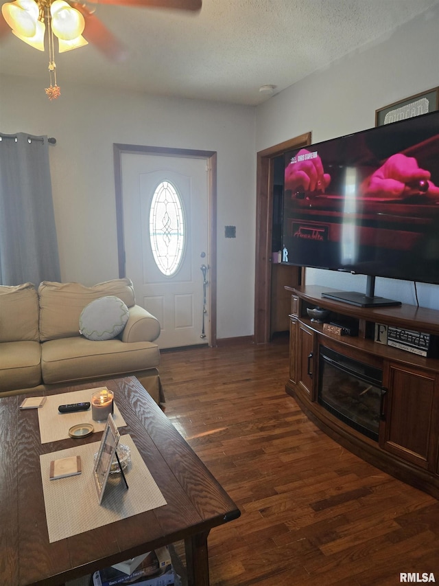 living room featuring dark wood-type flooring, ceiling fan, and a textured ceiling