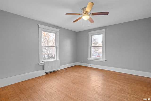 unfurnished room featuring ceiling fan, radiator heating unit, a wealth of natural light, and light wood-type flooring