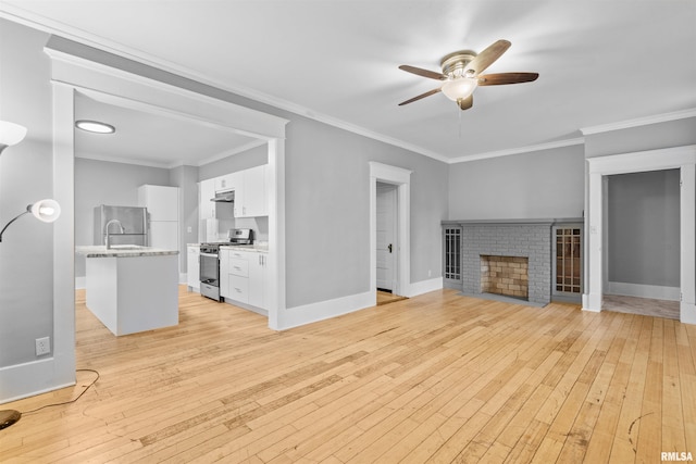 unfurnished living room featuring sink, ornamental molding, ceiling fan, a brick fireplace, and light wood-type flooring