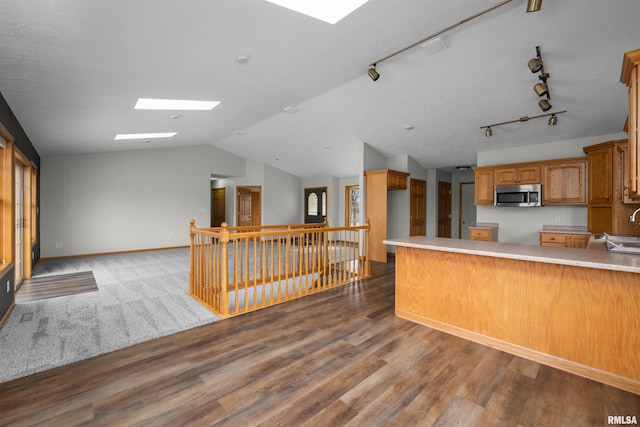 kitchen with lofted ceiling with skylight, hardwood / wood-style floors, rail lighting, sink, and kitchen peninsula