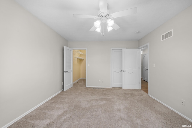 unfurnished bedroom featuring a spacious closet, light colored carpet, ceiling fan, and a closet