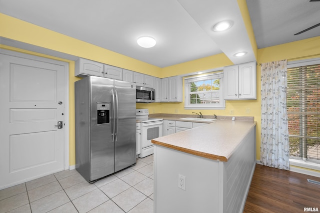 kitchen featuring sink, light tile patterned floors, white cabinetry, stainless steel appliances, and kitchen peninsula