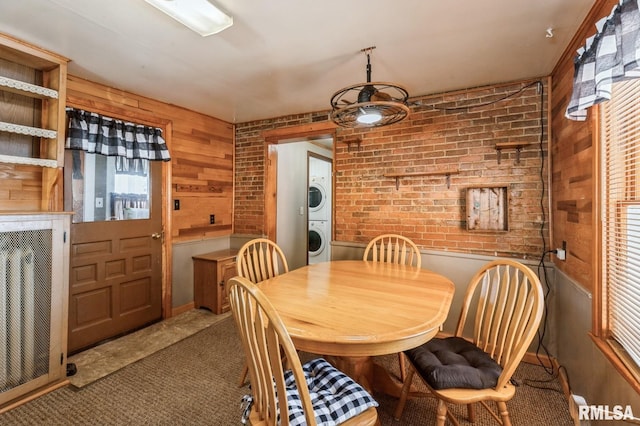 carpeted dining space with stacked washer and clothes dryer and wood walls