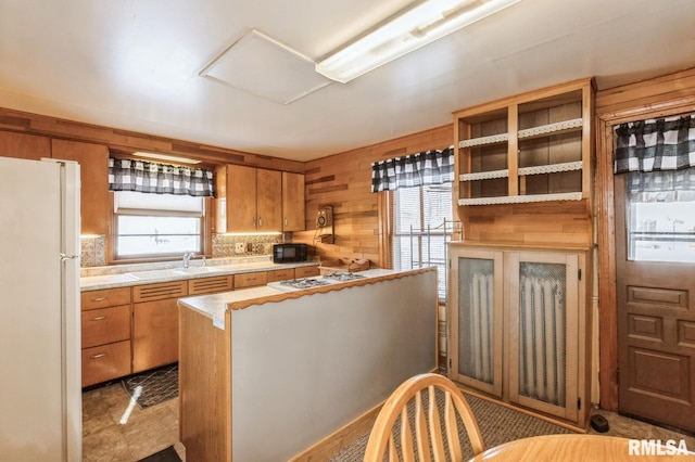 kitchen featuring white refrigerator, a healthy amount of sunlight, sink, and wooden walls