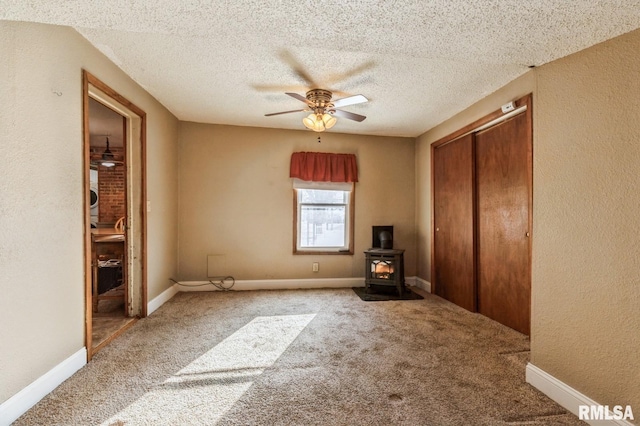 unfurnished bedroom featuring ceiling fan, a textured ceiling, light carpet, a closet, and a wood stove