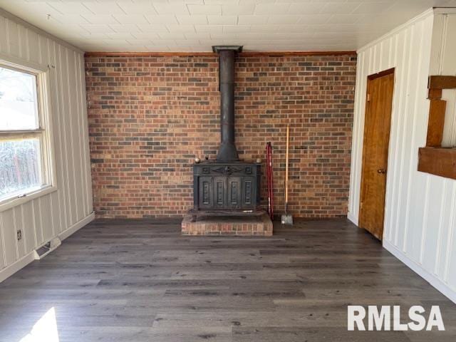 1615 Iowa Ave, Clinton, IA 52732 - unfurnished living room featuring a wood stove, wood finished floors, ornamental molding, and brick wall
