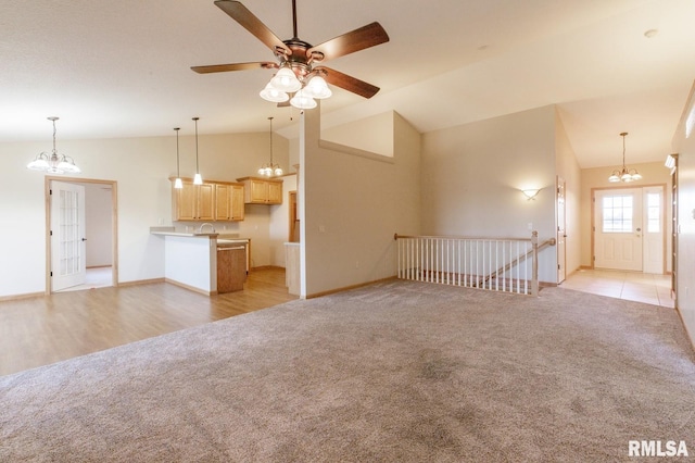 unfurnished living room featuring vaulted ceiling, ceiling fan with notable chandelier, and light colored carpet