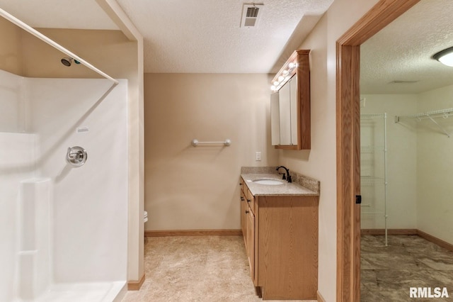 bathroom featuring vanity, a shower, a textured ceiling, and toilet