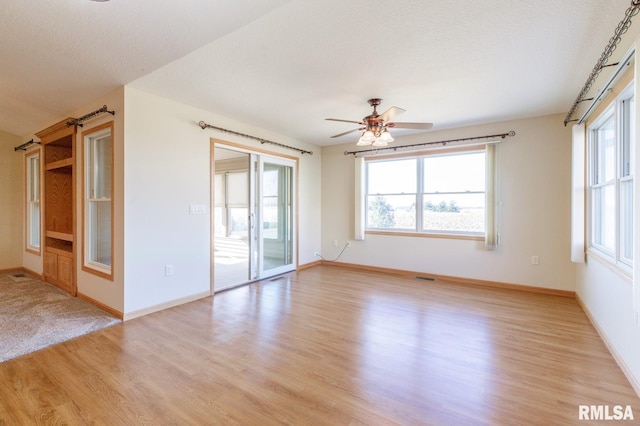 unfurnished room with ceiling fan, a textured ceiling, and light wood-type flooring