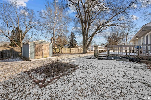 snowy yard with a wooden deck and a storage shed