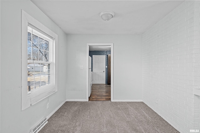 carpeted empty room featuring brick wall and plenty of natural light