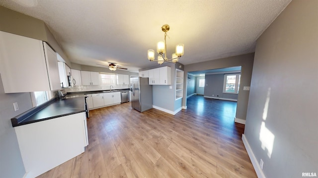 kitchen with pendant lighting, white cabinetry, stainless steel appliances, light hardwood / wood-style floors, and a textured ceiling