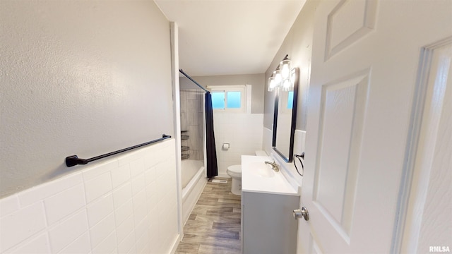 full bathroom with tiled shower / bath, hardwood / wood-style floors, tile walls, vanity, and toilet