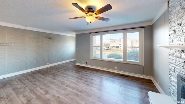 unfurnished room featuring ceiling fan, a fireplace, light hardwood / wood-style floors, a textured ceiling, and brick wall