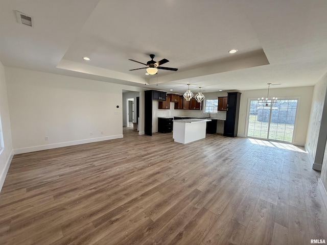 unfurnished living room featuring ceiling fan with notable chandelier, sink, hardwood / wood-style floors, and a tray ceiling