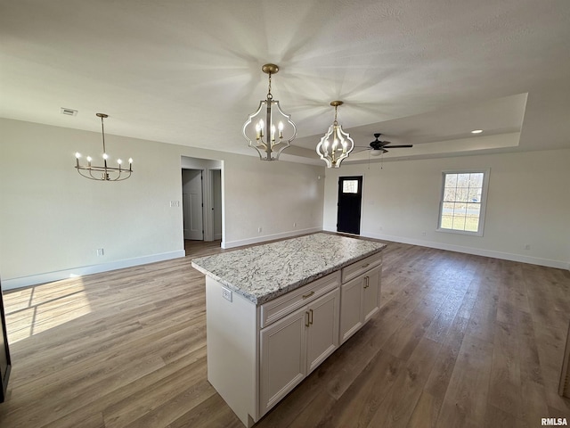 kitchen with white cabinetry, a tray ceiling, light stone counters, and decorative light fixtures