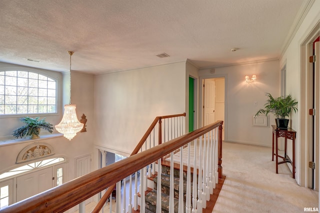 hall featuring an inviting chandelier, ornamental molding, light carpet, and a textured ceiling