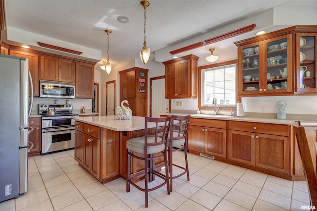 kitchen featuring sink, hanging light fixtures, a textured ceiling, a kitchen island, and stainless steel appliances