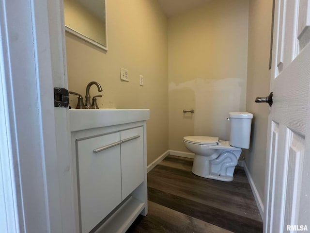 bathroom featuring toilet, baseboards, wood finished floors, and vanity