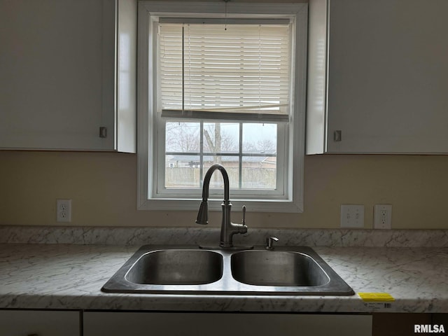 kitchen featuring light stone counters, sink, and white cabinets