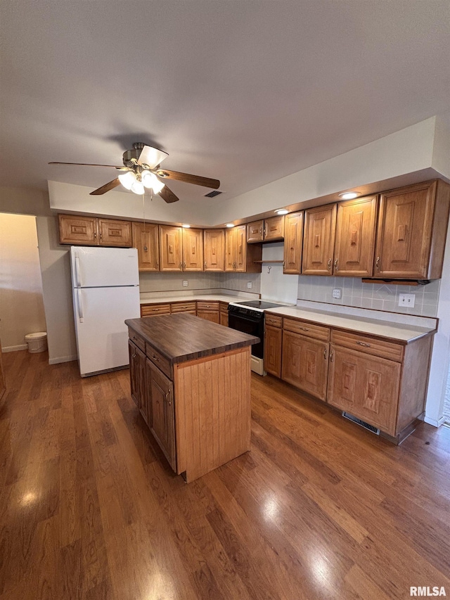 kitchen with black electric range oven, a kitchen island, dark hardwood / wood-style flooring, decorative backsplash, and white fridge