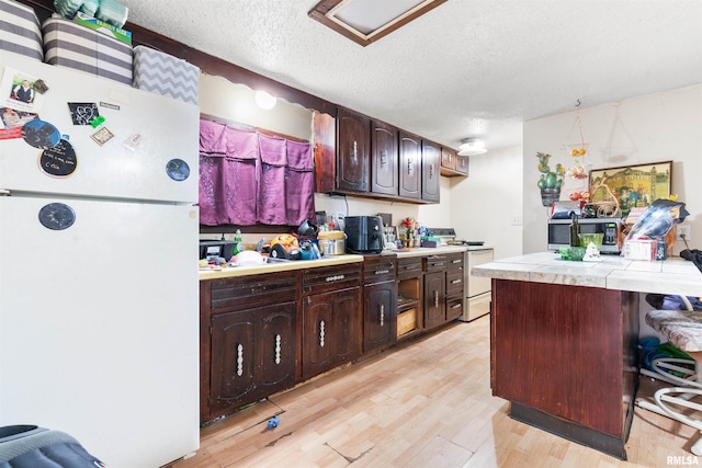 kitchen with a breakfast bar, tile countertops, dark brown cabinetry, stainless steel appliances, and a textured ceiling
