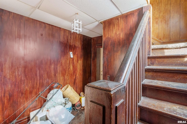 staircase featuring a drop ceiling, wood walls, and an inviting chandelier