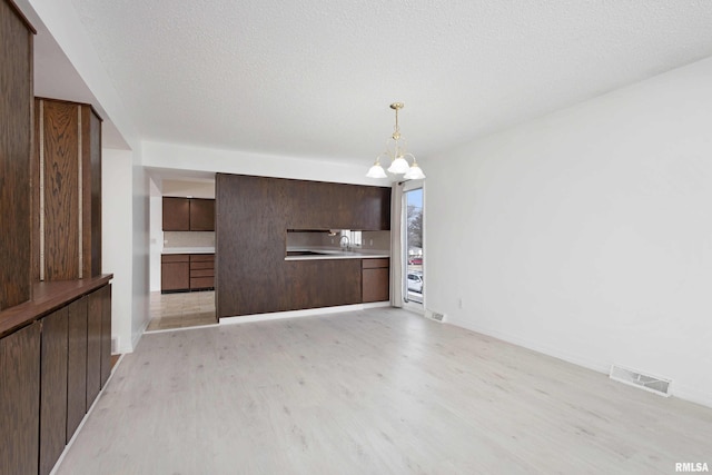 kitchen featuring hanging light fixtures, light hardwood / wood-style floors, dark brown cabinets, a textured ceiling, and an inviting chandelier