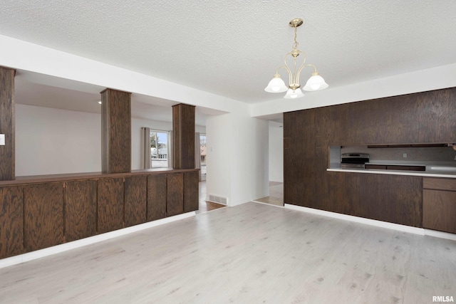 interior space with hanging light fixtures, dark brown cabinetry, a textured ceiling, a chandelier, and light wood-type flooring