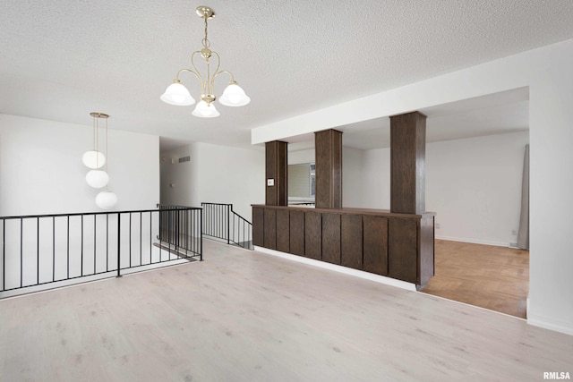 empty room with a textured ceiling, an inviting chandelier, and light hardwood / wood-style flooring