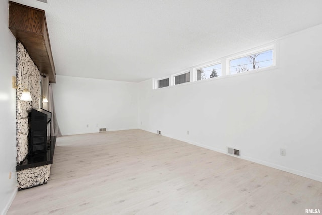 unfurnished living room featuring a fireplace, light hardwood / wood-style floors, and a textured ceiling