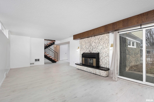 unfurnished living room featuring a stone fireplace, a healthy amount of sunlight, wooden walls, and a textured ceiling