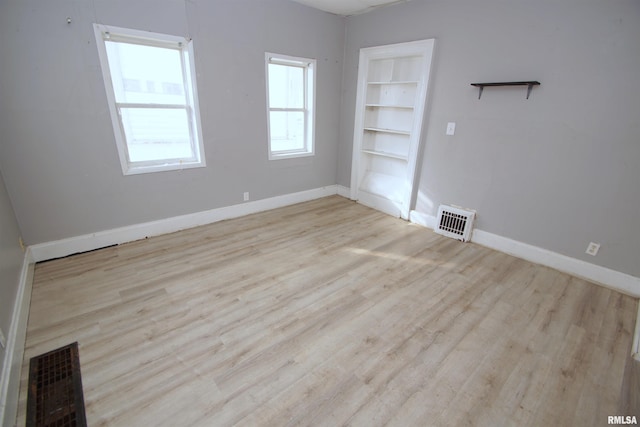 spare room featuring built in shelves and light wood-type flooring