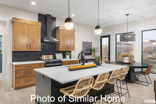 kitchen featuring wall chimney exhaust hood, decorative light fixtures, a center island with sink, black range, and decorative backsplash