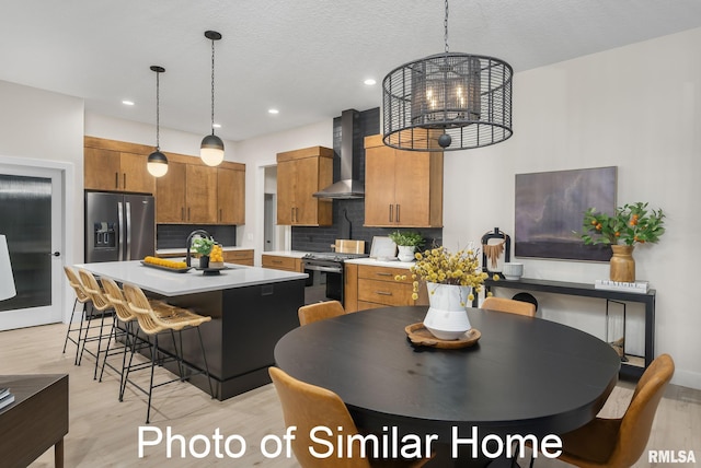 kitchen with wall chimney exhaust hood, stainless steel fridge with ice dispenser, hanging light fixtures, and stove