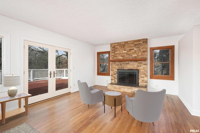 living room with a brick fireplace, hardwood / wood-style floors, a textured ceiling, and french doors