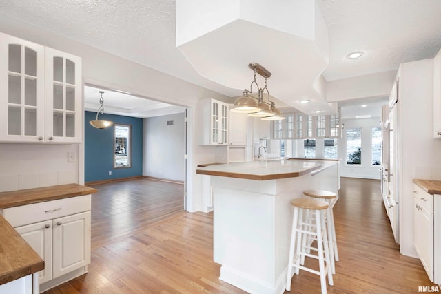 kitchen featuring an island with sink, white cabinets, wood counters, and decorative light fixtures