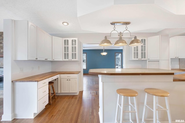 kitchen with wood counters, a breakfast bar, decorative light fixtures, kitchen peninsula, and white cabinets