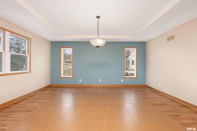 empty room featuring light tile patterned floors, a tray ceiling, and a textured ceiling