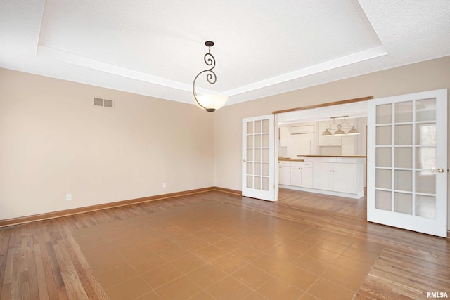 unfurnished room featuring a raised ceiling, a textured ceiling, and french doors