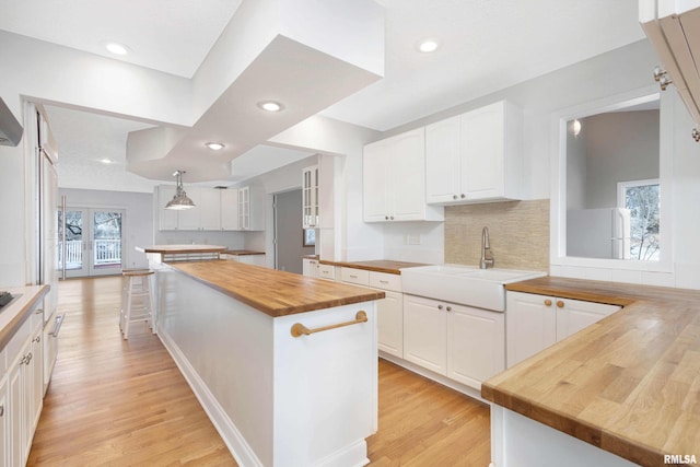 kitchen with wood counters, sink, a kitchen island, and white cabinets