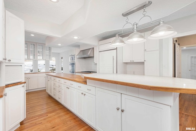 kitchen with white cabinetry, a textured ceiling, hanging light fixtures, decorative backsplash, and wall chimney range hood