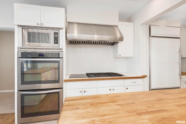 kitchen featuring wall chimney range hood, wood-type flooring, stainless steel appliances, and white cabinets