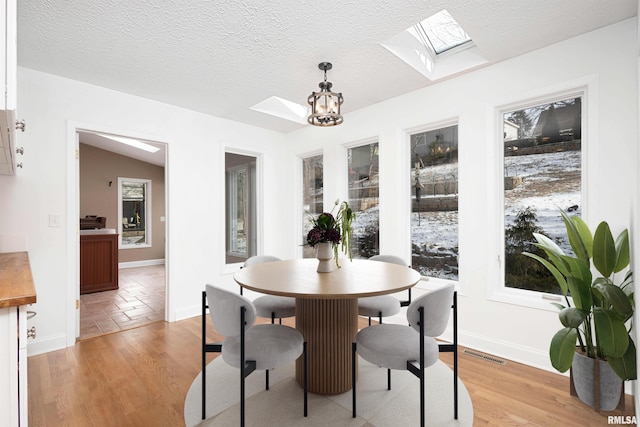 dining space featuring a chandelier, vaulted ceiling with skylight, a textured ceiling, and light hardwood / wood-style flooring