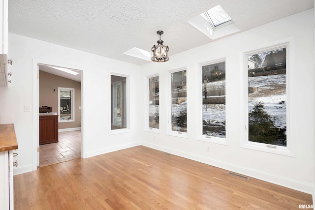 unfurnished dining area with an inviting chandelier, lofted ceiling with skylight, hardwood / wood-style floors, and a textured ceiling