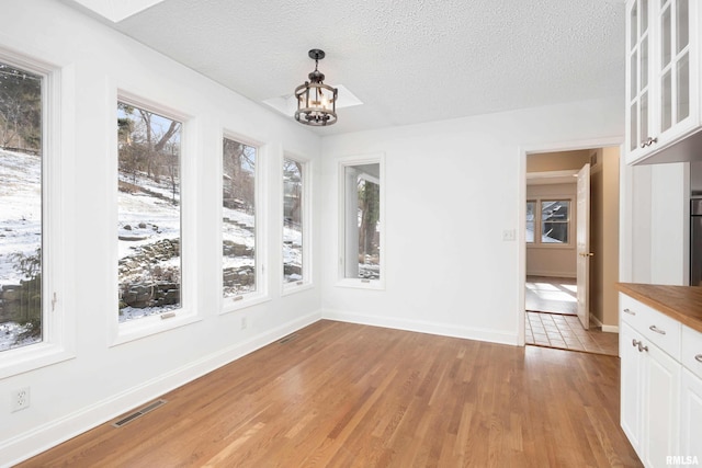 unfurnished dining area with a chandelier, a textured ceiling, and light hardwood / wood-style floors