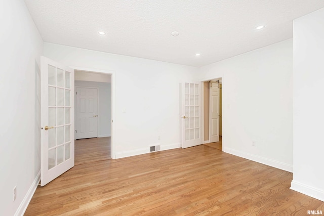 empty room featuring french doors, light hardwood / wood-style flooring, and a textured ceiling