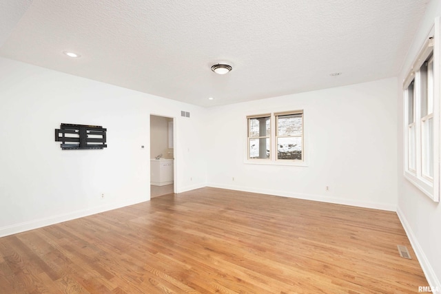 empty room with a healthy amount of sunlight, a textured ceiling, and light hardwood / wood-style flooring