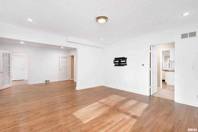 unfurnished room featuring light hardwood / wood-style flooring, french doors, and a textured ceiling